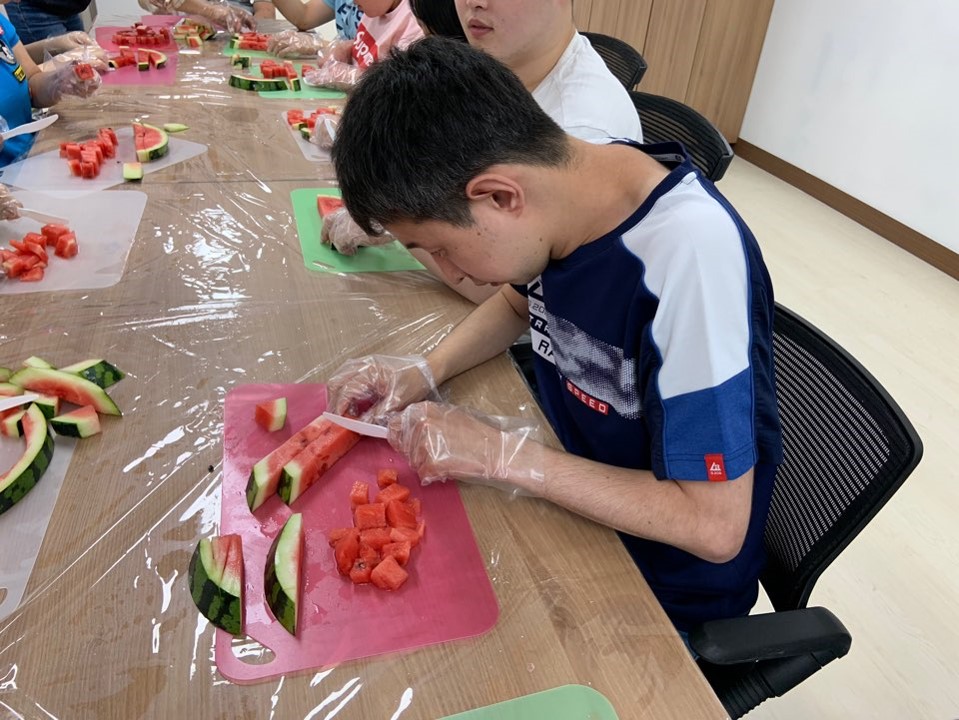 주간보호센터 이용자가 수박을 알맞는 크기로 자르기 위해 집중을 하고 있는 모습