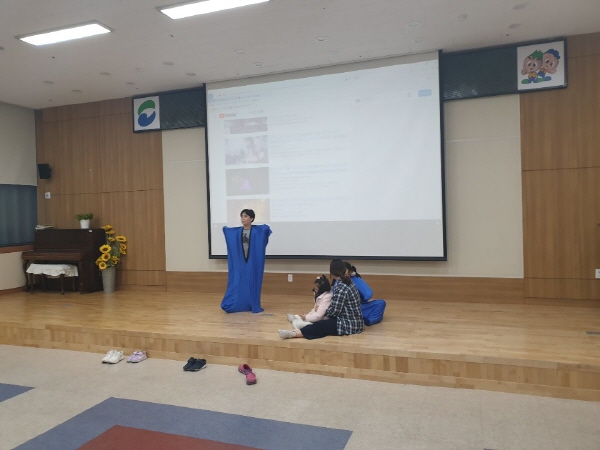 아이들이 천을 두르고 있고 보조강사와 두명의 아이가 앉아서 이야기를 하는 모습
