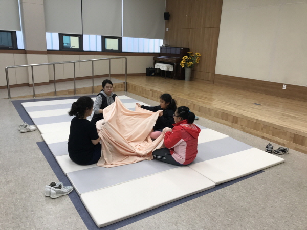 강사와 아이들이 둥글게 앉아 천을 활용한 활동을 진행하는 모습